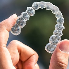 A hand holding an Invisalign tray between two fingers