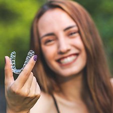 A beautiful, smiling woman holding an Invisalign tray