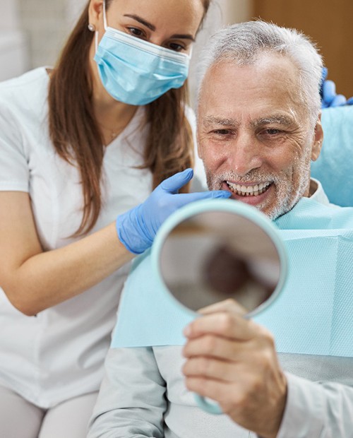 An elderly man admiring his new dental implants in a hand mirror
