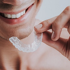 A smiling man holding a transparent mouthguard